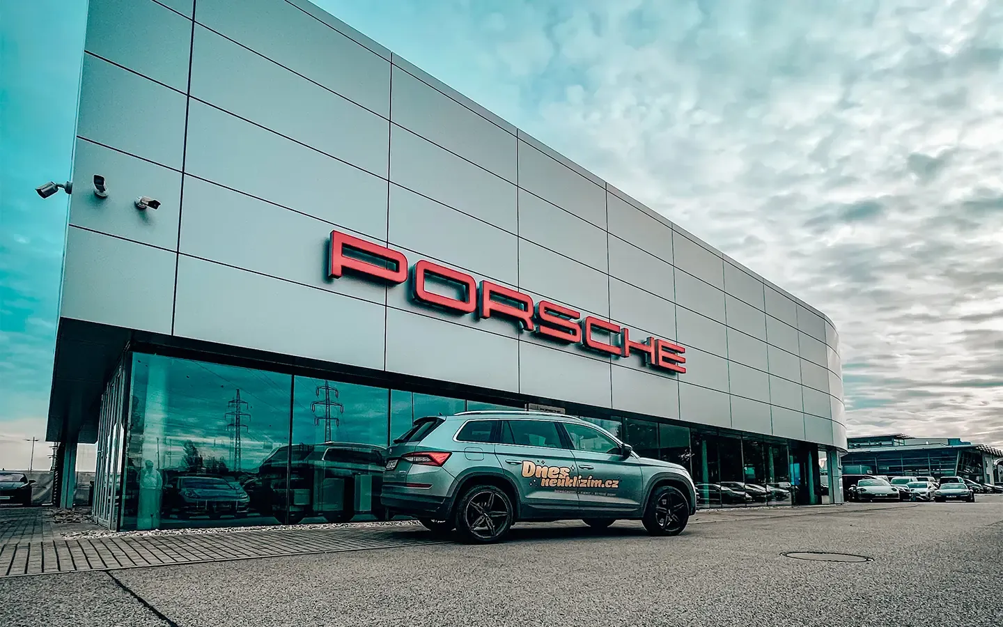 Umytá prosklená fasáda autosalonu Porsche s firemním vozem Dnes Neuklízím
